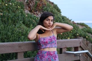 Anusha Mitra is a 3rd year Biopsychology major who works at the Women's Center as a programmer. she is pictured here by the beach stairs, framing her face with her hands. 